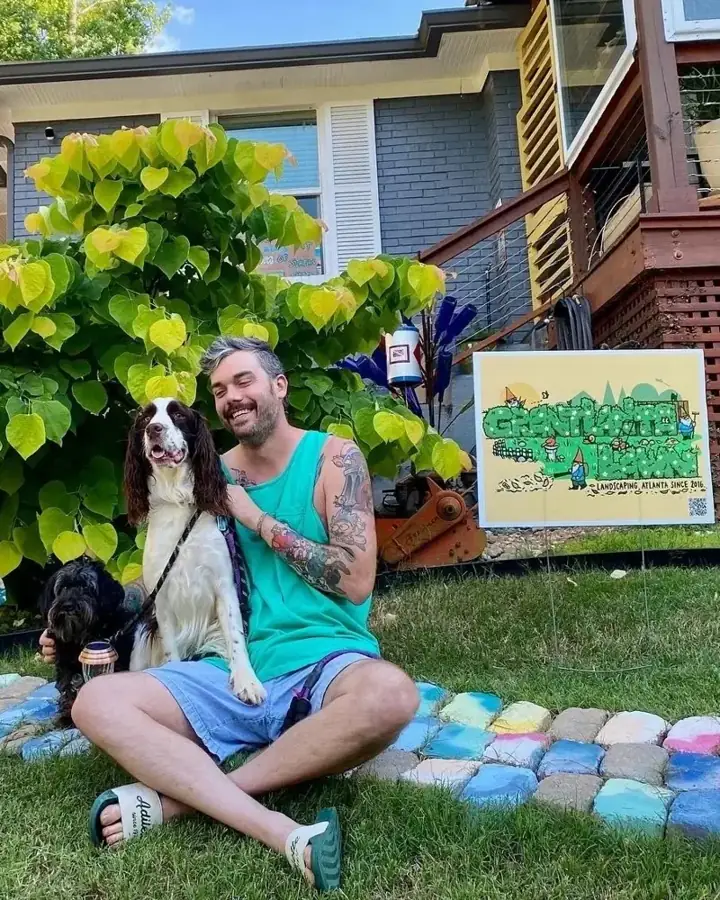 Grant Wallace, owner of Grantlanta Lawn, with his two dogs in a front yard next to the Grantlanta sign